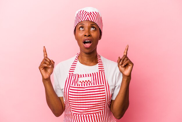 Giovane donna afroamericana del gelatiere isolata su fondo rosa che indica al rialzo con la bocca aperta.