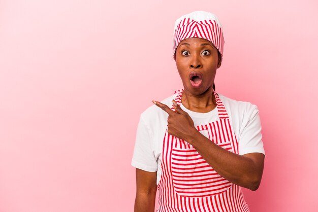 Giovane donna afroamericana del gelatiere isolata su fondo rosa che indica il lato