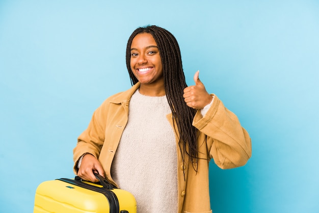 Giovane donna afroamericana del viaggiatore che tiene una valigia che sorride e che alza pollice in su