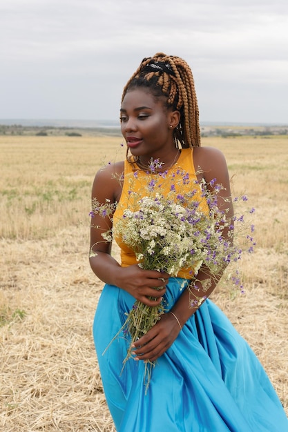 Giovane donna afroamericana divertendosi all'aperto al tramonto ragazza che ride sul campo bouquet di fiori selvatici bella giovane donna afroamericana con le trecce