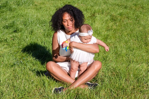Giovane donna afroamericana e sua figlia che si siedono sull'erba verde nel parco estivo.