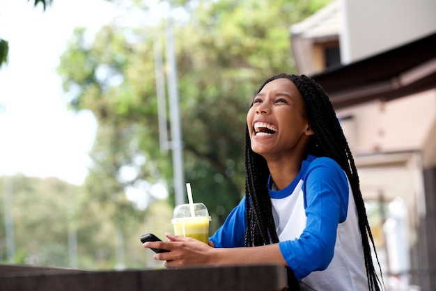 Giovane donna afroamericana felice con il telefono cellulare al caffè