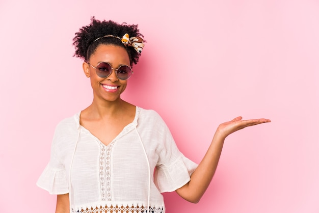 Giovane donna afroamericana hipster isolata mostrando uno spazio di copia su un palmo e tenendo un'altra mano sulla vita.