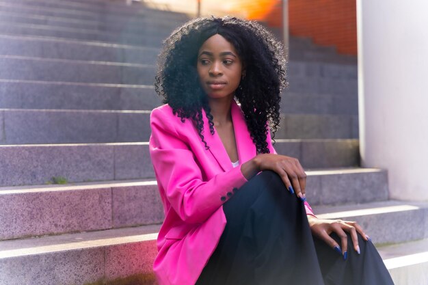 Giovane donna afroamericana in città Ritratto di giovane donna in giacca rosa seduta