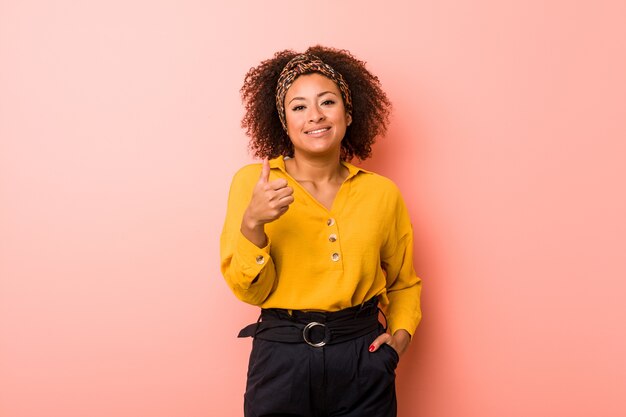 Giovane donna afroamericana in rosa sorridente e alzando il pollice