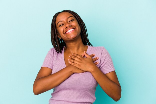 Giovane donna afroamericana isolata su fondo blu che ride tenendo le mani sul cuore, concetto di felicità.