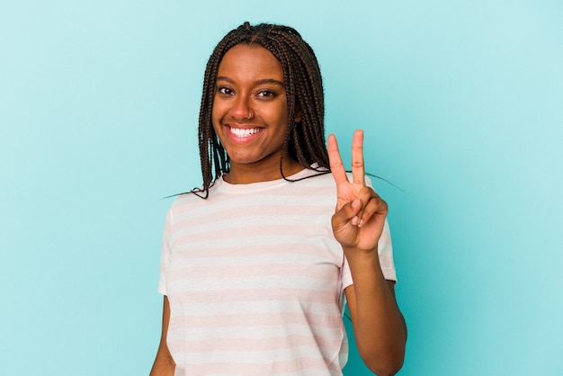 Giovane donna afroamericana isolata su fondo blu gioiosa e spensierata che mostra un simbolo di pace con le dita.