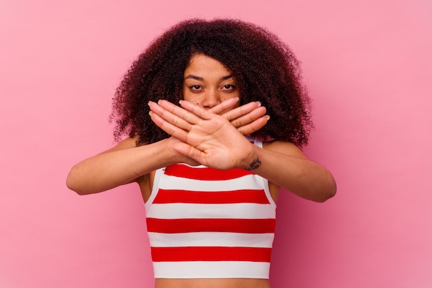 Giovane donna afroamericana isolata su fondo rosa che fa un gesto di rifiuto