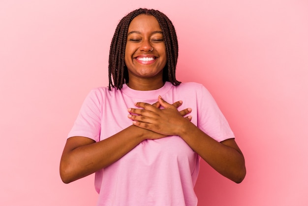 Giovane donna afroamericana isolata su fondo rosa che ride tenendo le mani sul cuore, concetto di felicità.