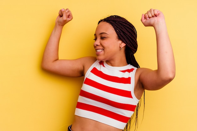 Giovane donna afroamericana isolata su giallo che celebra un giorno speciale, salta e alza le braccia con energia.