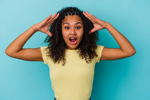 Giovane donna afroamericana isolata su sfondo blu che celebra una vittoria o un successo, è sorpreso e scioccato.