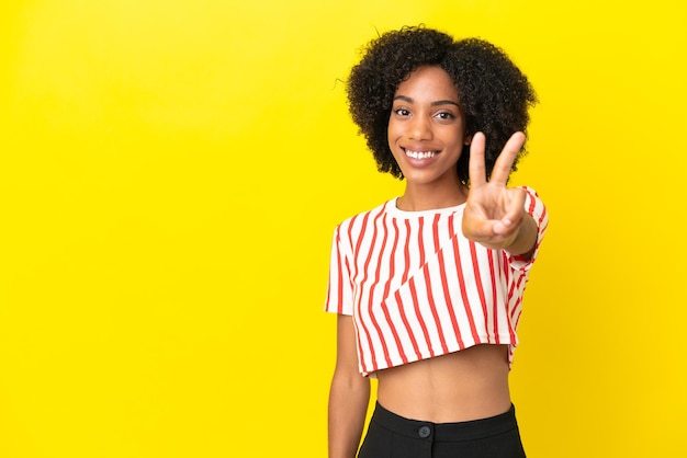Giovane donna afroamericana isolata su sfondo giallo sorridente e mostrando il segno della vittoria