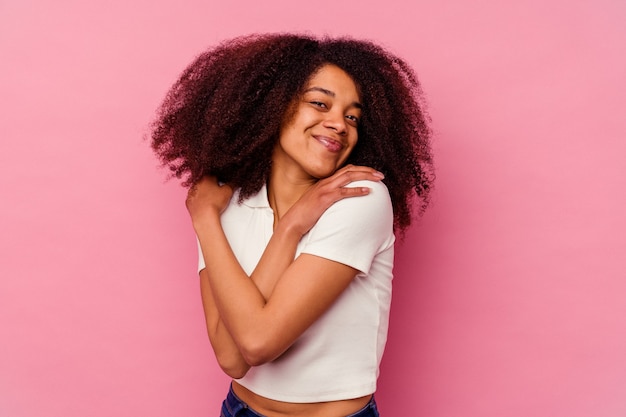 Giovane donna afroamericana isolata su sfondo rosa abbracci, sorridente spensierata e felice.