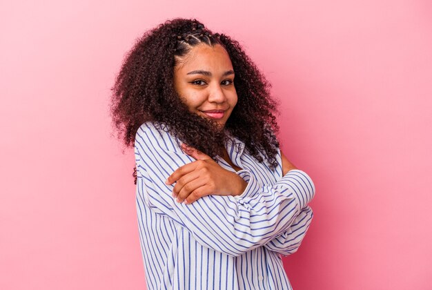 Giovane donna afroamericana isolata su sfondo rosa abbracci, sorridente spensierata e felice.
