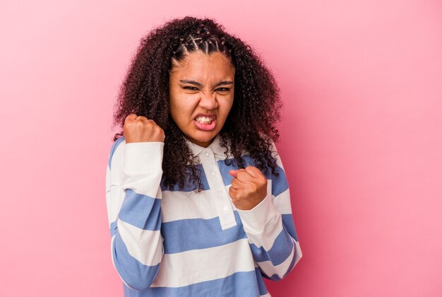 Giovane donna afroamericana isolata su sfondo rosa che mostra pugno alla telecamera, espressione facciale aggressiva.