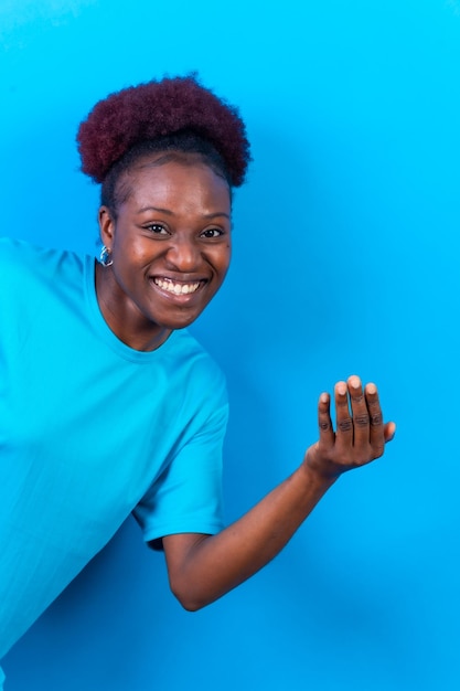 Giovane donna afroamericana isolata su uno sfondo blu che invita a venire con la mano
