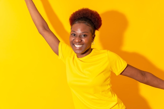 Giovane donna afroamericana isolata su uno sfondo giallo che sorride e balla le riprese in studio