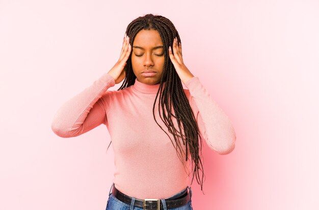 Giovane donna afroamericana isolata su uno sfondo rosa, toccando le tempie e avendo mal di testa.