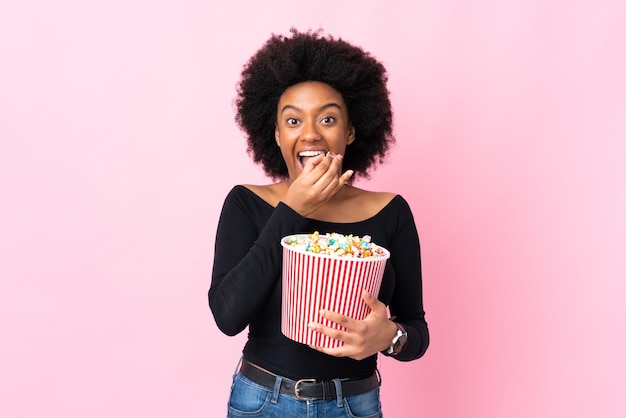 Giovane donna afroamericana isolata sul colore rosa che tiene un grande secchio di popcorn