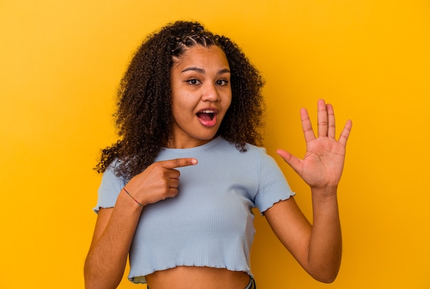 Giovane donna afroamericana isolata sul muro giallo sorridente allegro che mostra il numero cinque con le dita