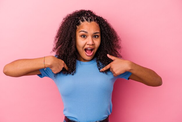 Giovane donna afroamericana isolata sul muro rosa sorpreso indicando con il dito, sorridendo ampiamente