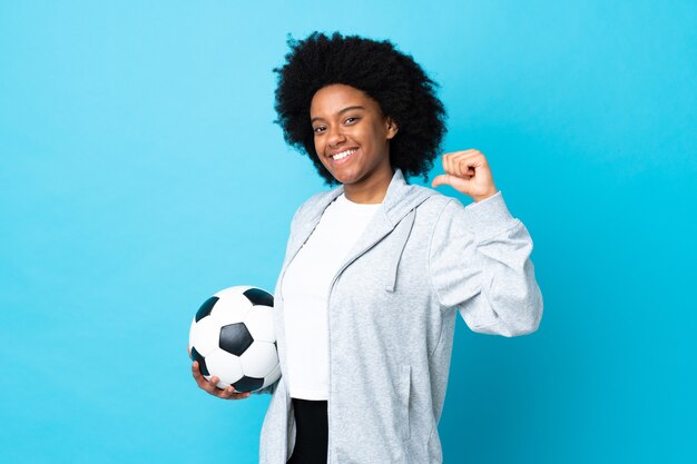 Giovane donna afroamericana isolata sull'azzurro con pallone da calcio e orgoglioso di se stesso