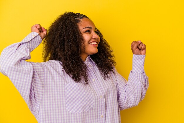 Giovane donna afroamericana isolata sulla parete gialla che celebra un giorno speciale, salta e alza le braccia con energia