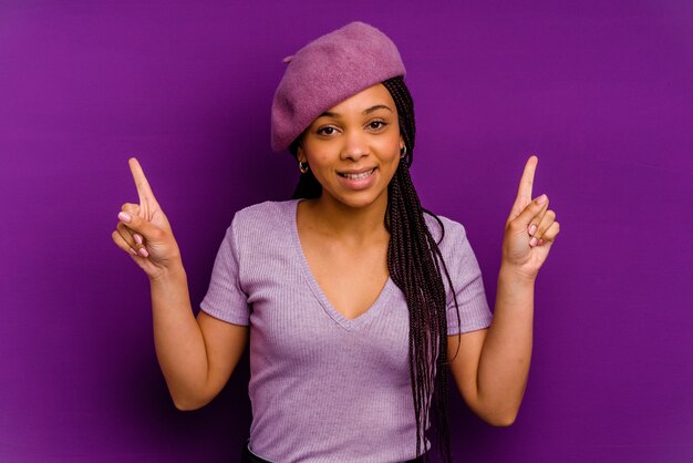 Giovane donna afroamericana isolata sulla parete gialla che punta a diversi spazi di copia, scegliendo uno di loro, mostrando con il dito