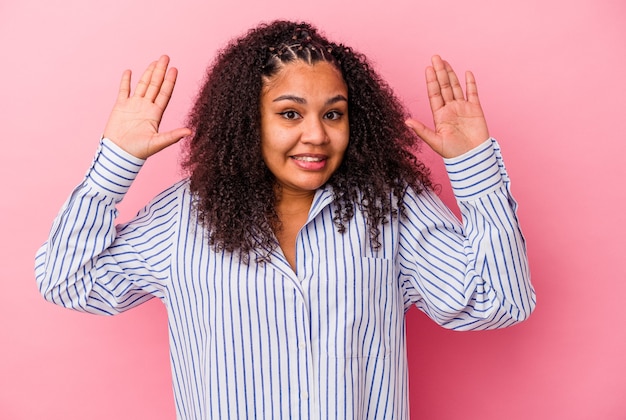 Giovane donna afroamericana isolata sulla parete rosa che riceve una piacevole sorpresa, eccitata e alzando le mani.