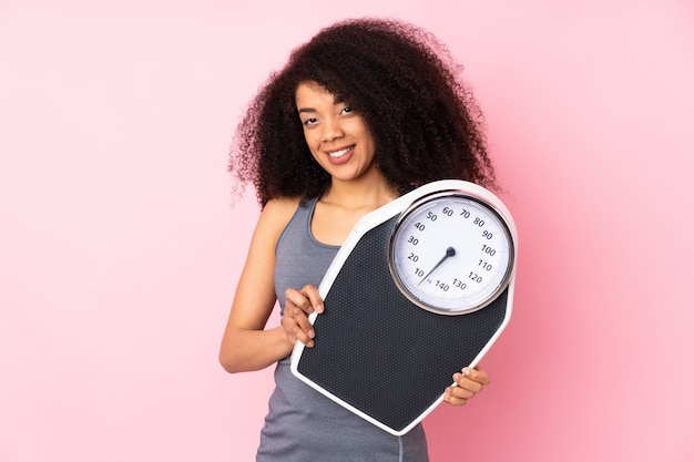 Giovane donna afroamericana isolata sulla parete rosa con la pesa