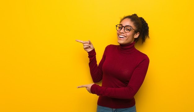 Giovane donna afroamericana nera con gli occhi azzurri che punta al lato con il dito