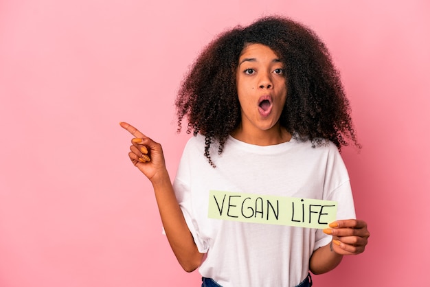 Giovane donna afroamericana riccia che tiene un cartello di vita vegano che punta al lato