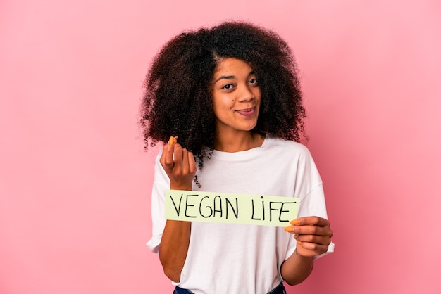 Giovane donna afroamericana riccia che tiene un cartello di vita vegano che punta con il dito contro di te come se invitando ad avvicinarsi