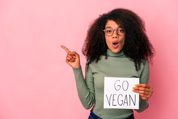 Giovane donna afroamericana riccia che tiene un cartello vegano che punta di lato