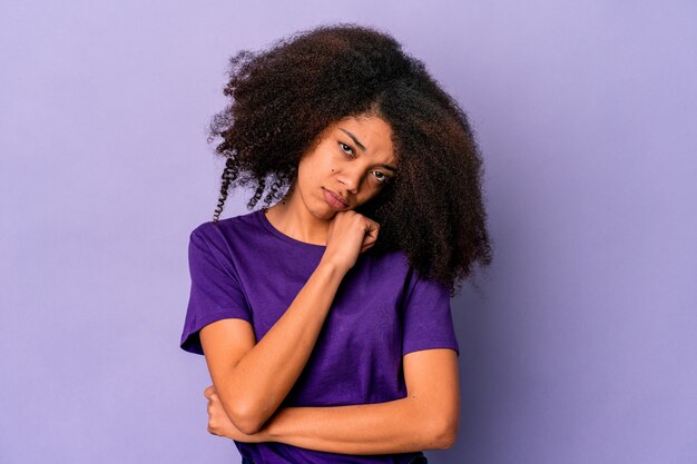 Giovane donna afroamericana riccia isolata su sfondo viola stanca di un compito ripetitivo.
