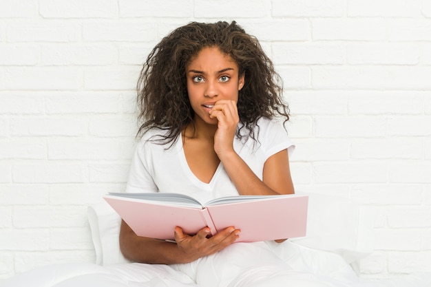 Giovane donna afroamericana seduta sul letto a studiare le unghie mordaci, nervosa e molto ansiosa.