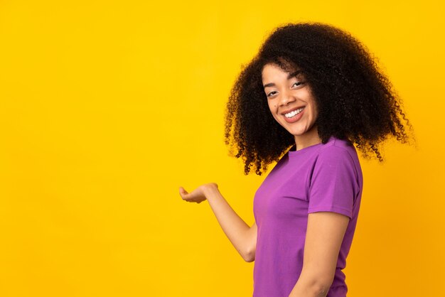 Giovane donna afroamericana sopra la parete che estende le mani al lato