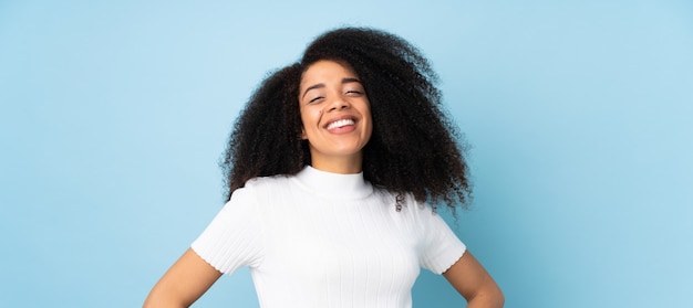 Giovane donna afroamericana sopra la parete che posa con le armi all'anca e al sorridere