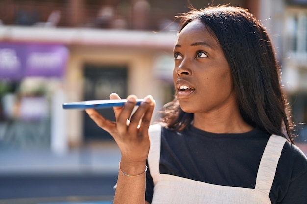 Giovane donna afroamericana sorridente che parla fiducioso sullo smartphone in strada