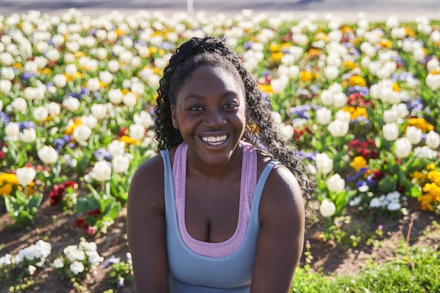 Giovane donna afroamericana sorridente seduta a guardare la telecamera circondata da fiori colorati