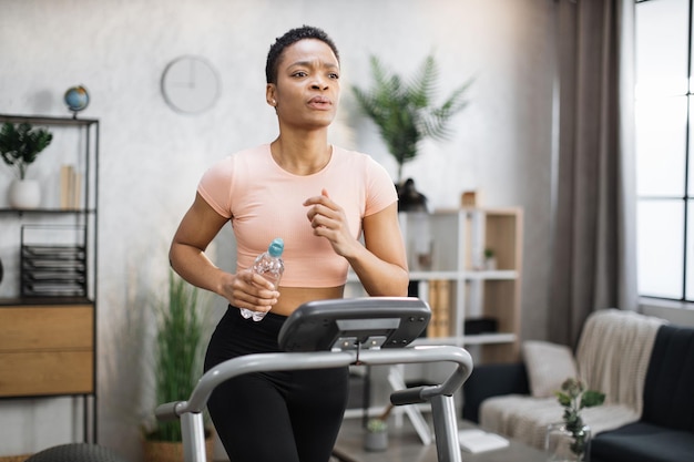 Giovane donna afroamericana sportiva attraente che tiene la bottiglia con l'acqua che risolve