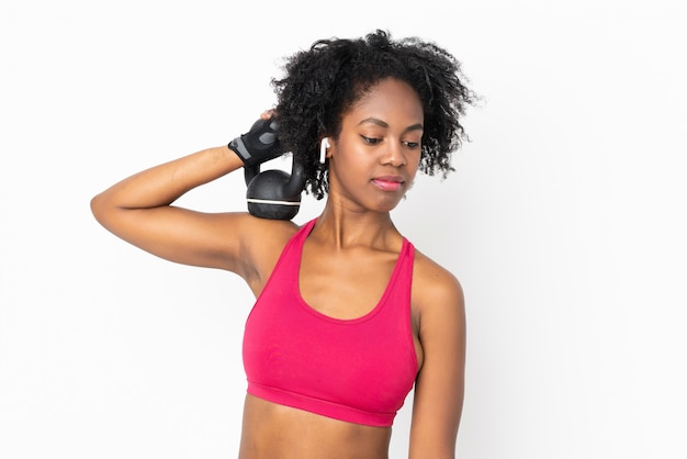 Giovane donna afroamericana sulla parete bianca che fa sollevamento pesi con kettlebell