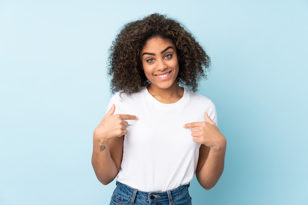 Giovane donna afroamericana sulla parete blu che punta a se stessi