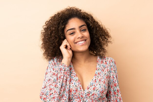 Giovane donna afroamericana sulla risata beige della parete