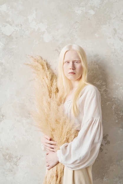 Giovane donna albina serena in camicetta bianca che tiene mazzo di fiori secchi