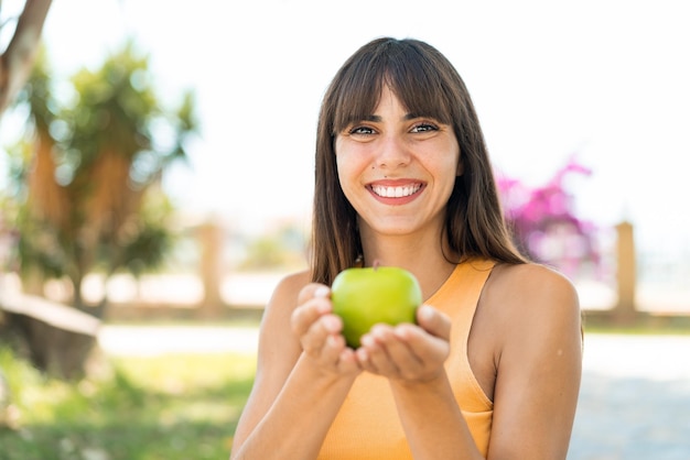 Giovane donna all'aperto che tiene una mela con un'espressione felice