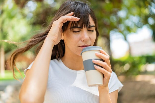 Giovane donna all'aperto con mal di testa e tenendo un caffè da asporto