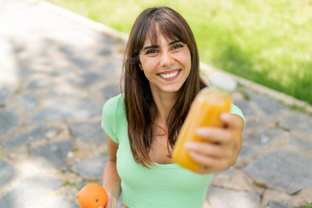 Giovane donna all'aperto con un'arancia e un succo d'arancia