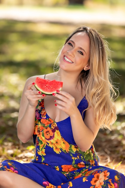 Giovane donna all'aperto sotto gli alberi in un parco, felice e sorridente, facendo pic nic e degustazione di anguria.