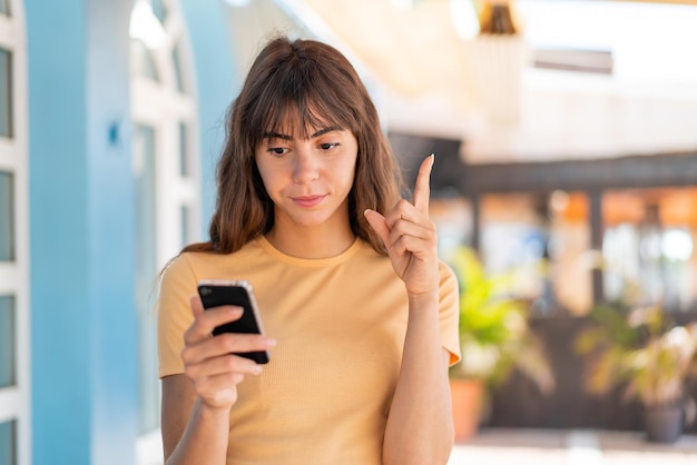 Giovane donna all'aperto utilizzando il telefono cellulare e il dito di sollevamento